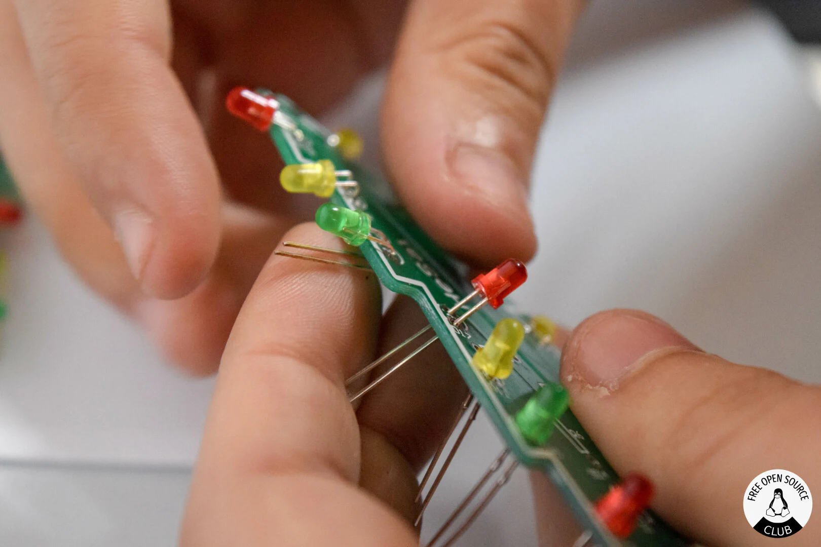 Many LEDs with long legs being placed in a tree shaped PCB
